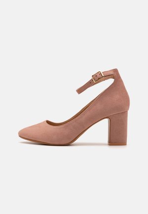 Chaussure à talon haut en daim rose avec un bout arrondi, une sangle ajustable à la cheville et un talon bloc. Caractérisée par une texture lisse et des détails minimaux.