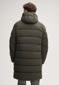 Parka imbottita di un verde scuro, caratterizzata da un colletto alto, cuciture orizzontali e una silhouette lunga, progettata per calore e comfort.