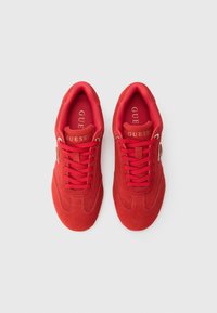 Piros színű vászoncipő bársony hatással, lekerekített orral, lapos fűzőkkel és arany színű logóval az oldalon. Minimalista kialakítás.