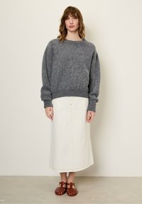 Siv pleten pulover z okroglo odprtino in dolgimi, ohlapnimi rokavi, v kombinaciji s smetanasto, krilom do kolen in rjavimi, pasnatimi sandali.