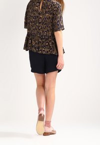 Krótki rękaw, top peplum w zielono-granatowy wzór zwierzęcy z dekoltem w kształcie łezki, zestawiony z granatowymi szortami do kolan i beżowymi butami na kostkę.