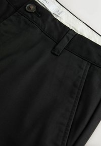 Pantalon noir avec fermeture par bouton et passants de ceinture, montrant la ceinture et une partie du détail de la poche avant.