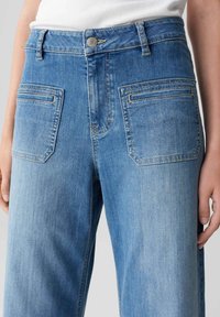 Helle blaue Jeans mit hoch tailliertem Design, ausgestattet mit vorderen und hinteren Taschen, sanften Ausbleichungen und einem Metallknopfverschluss.