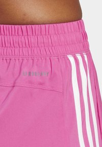 Pantalones cortos deportivos rosas con una cintura elástica, que presentan un logo plateado "AEROREADY" y tres rayas blancas en los laterales. Textura de tela suave.