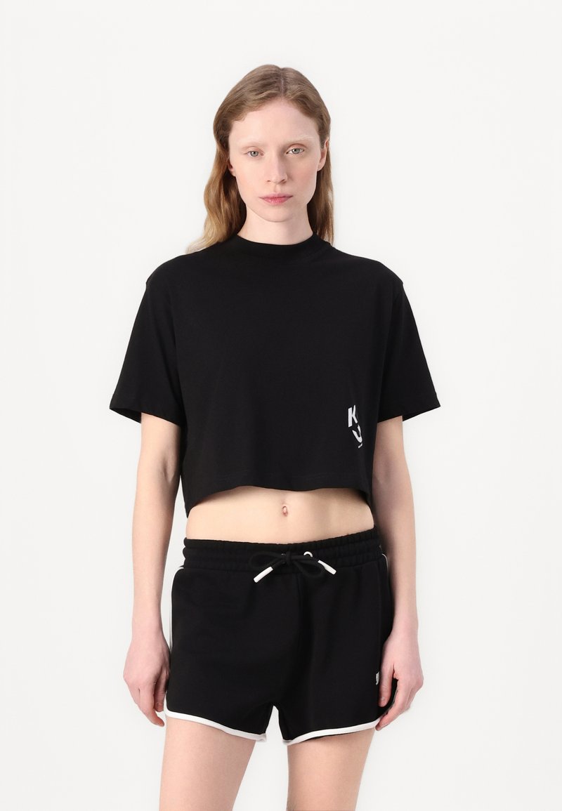 Svart croppet t-skjorte med korte ermer og rund hals, med en liten hvit grafisk logo. Kombinert med svarte shorts med snor.