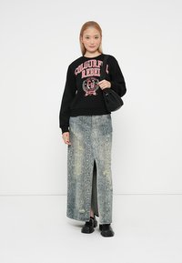 Zwarte sweater met roze grafische tekst, gecombineerd met een lange, lichtblauwe slangenprintrok met een split. Zwarte chunky schoenen en een tas.