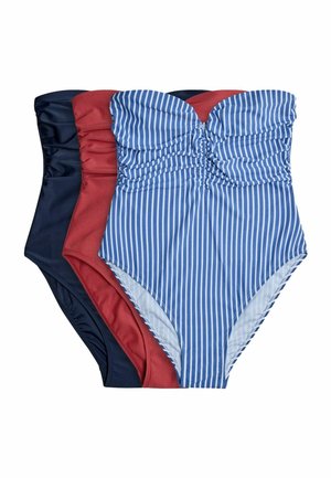 Žena pózuje na jednofarebnom pozadí v modro-bielom jednodielnom plavkách so zvislými pruhmi bez ramienok.