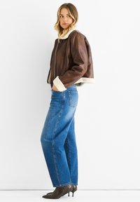 Brown leather cropped jacket with white shearling collar and cuffs, paired with blue straight-leg jeans and pointed snake-print heels.