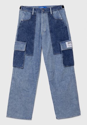 Denim cargo bukser med lyse og mørke blå paneler, to sidelommer, vid benpassform og synlige sømdetaljer. Merket med et etikett foran.