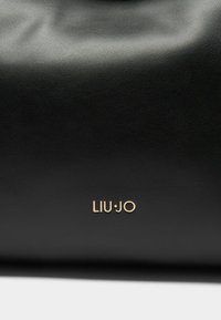 Bolso de mano de cuero negro con textura suave y logo en relieve en fuente dorada: "LIU·JO" centrado en el panel frontal inferior.