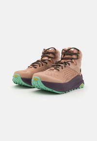 Lette fotturesko for fotturer med en ferskenfarget overdel, brune snører, en lilla mellomsåle og en grønn Vibram yttersåle med teksturert grep.