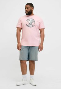 Roosa puuvillane t-särk musta ja sinise graafilise kolju kujundusega, kombineerituna heledate teksashortsidega ja valgete tossudega.