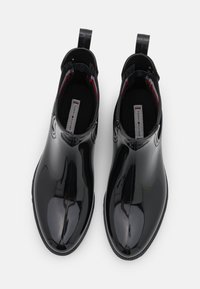 Bottines noires imperméables avec une finition brillante, des tirettes et une doublure en tissu contrasté, présentant un design lisse et élégant.