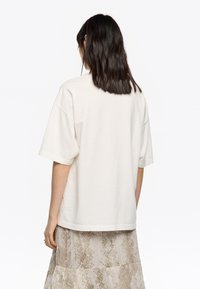 Kremowy bawełniany t-shirt z krótkim rękawem, luźny krój i zaokrąglony dół, nałożony na lekką, teksturowaną, wzorzystą spódnicę.