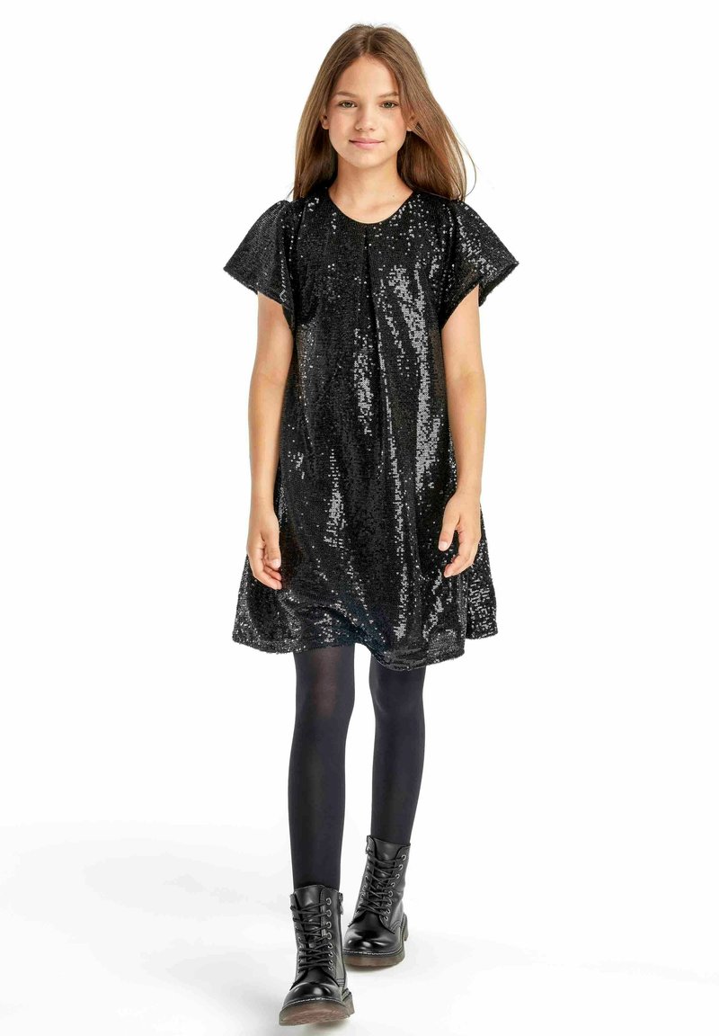 Robe en sequins noirs à manches courtes, silhouette fluide, col rond, assortie à des collants noirs et des bottes de combat à lacets.
