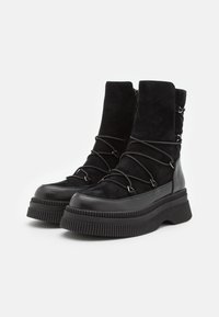 Zwarte laarzen met een mix van suede en leer, een chunky rubberen zool, veters aan de voorkant en een ritssluiting aan de achterkant.