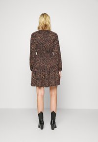 Robe noire à fleurs présentant des manches longues, une taille élastique et une jupe évasée, assortie à des bottes noires brillantes à la cheville.