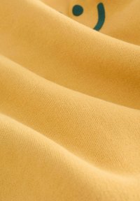 Gelbes Gewebe mit einer glatten Textur, das blaue Druckakzente und einen leichten Stretch aufweist. Nahaufnahme, die die Weichheit und Farbintensität betont.