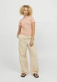 T-shirt a righe nei colori rosa e giallo, maniche corte. Pantaloni larghi beige con vita regolabile. Modello che indossa ciabatte nere.