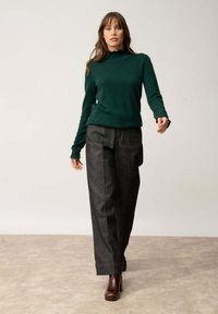 Maglione a collo alto a maglia verde scuro abbinato a pantaloni in denim scuro a vita alta, con cuciture a contrasto e vestibilità rilassata. Stivali con tacco marroni.