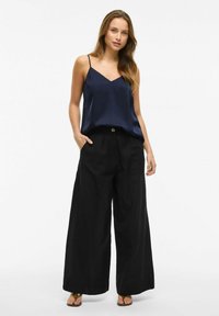 Granatowa satynowa koszulka na ramiączkach z cienkimi paskami, w zestawie z luźnymi czarnymi spodniami o szerokich nogawkach. Spodnie mają zapięcie na guzik z przodu oraz kieszenie.