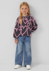 Maglione grigio lavorato a maglia con motivi a cuore rosa, abbinato a jeans nuovi a gamba larga blu. Il modello indossa sneakers bianche e ha capelli biondi lisci.