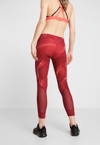 Czerwone legginsy sportowe z graficznym wzorem, z siateczkowymi wstawkami na dolnej części nóg i zamkami po bokach. Połączenie z kontrastowym stanikiem sportowym.