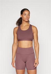 Burgundo spalvos sportinė crop tipo marškinėliai ir aukšto liemens šortai, pagaminti iš elastingos medžiagos, turintys lygią tekstūrą ir minimalų siuvimo detalių kiekį.
