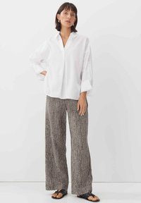 Witte langemouwen shirt met een V-hals, gecombineerd met zwart-witte geblokte wijde broek. Sandalen maken de outfit compleet.