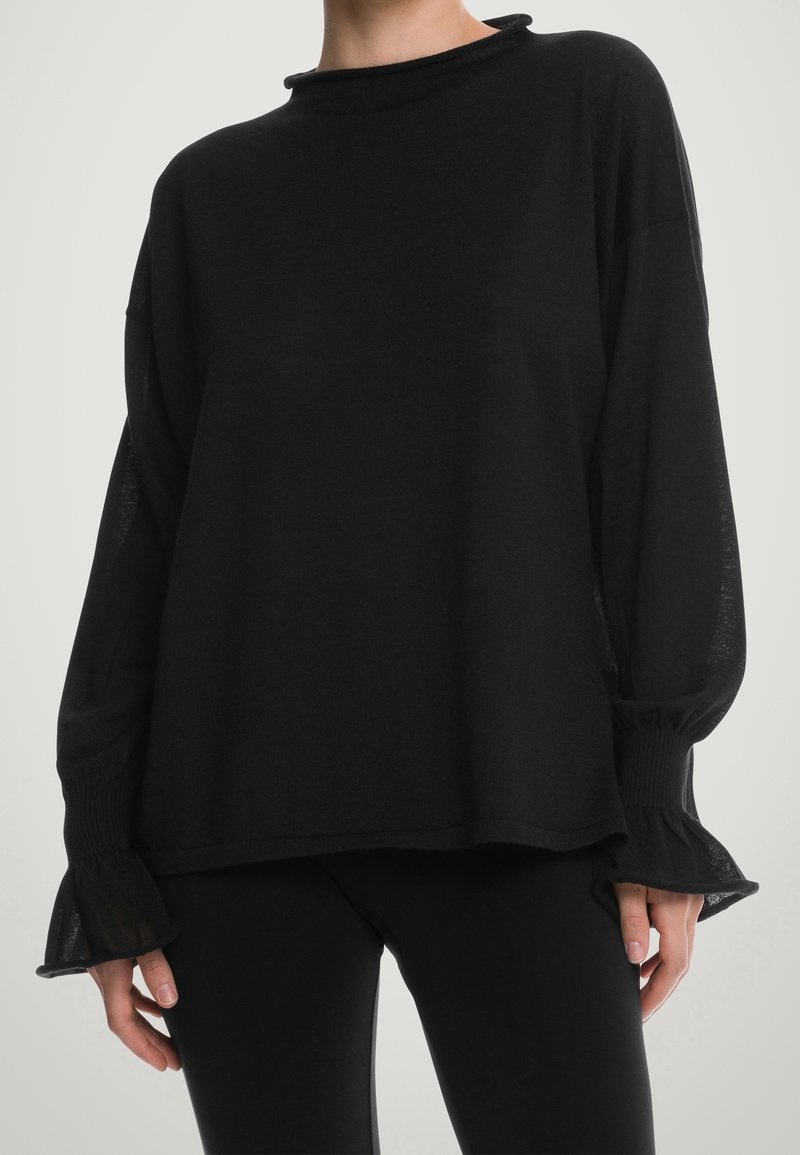 Svart långärmad tröja med en lös passform, hög krage, ribbade ärmslut och genomskinliga, utsvängda ärmar. Materialet verkar mjukt och lätt.