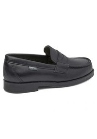 Zapato mocasín de cuero negro con puntera redondeada, detalles cosidos y suela plana de goma. Cuenta con una correa decorativa en la parte frontal.