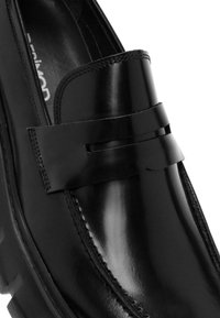 Zwarte leren loafer met een gladde, glanzende afwerking, voorzien van een horizontale accentband en gedetailleerde stiksels langs de randen.