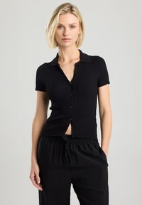 Black ribbed short-sleeve button-up top with a collar and a slight V-neck design. The fabric appears soft and textured.