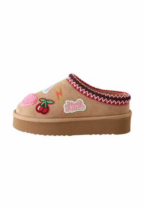 Tan suede clog with a textured finish, colorful embroidered patches, a brown rubber sole, and a red and white stitched trim along the edge.