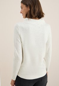 Vit tröja med mjukt material, med en cowl-hals, långa ärmar och ett fläckigt mönster för extra detaljer.