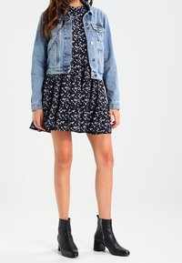 Jeansjacka över en marinblå blommig klänning, svarta ankelboots. Klänningen har en utsvängd design med små vita blommor; jackan har knapppdekorationer.