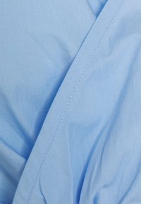 Tessuto di cotone blu chiaro con una texture liscia, caratterizzato da leggere pieghe e un dettaglio di cucitura. Design semplice e privo di pattern.