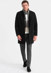 Abrigo de lana negro con diseño de doble botonadura, bufanda gris con patrón de espiga, suéter blanco y pantalones grises de corte ajustado.