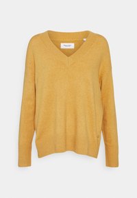Sweter oversize w kolorze musztardowym z dekoltem w kształcie litery V. Miękka, teksturowana tkanina z prążkowanymi mankietami i dołem. Metka widoczna wewnątrz kołnierza.