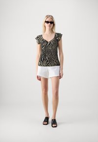 Svart og gull zebra mønster topp med volangerm sleeves, kombinert med hvite, frynsete shorts og svarte åpen-tå mules. En enkel og avslappet antrekk.