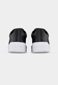 Ζευγάρι μαύρα sneakers χαμηλού ύψους με επενδυμένες επενδύσεις στον αστράγαλο και χοντρές λευκές σόλες με ανάγλυφη την επιγραφή "LOVE MOSCHINO" που φαίνονται από πίσω.