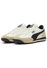 Witte leren en beige suède sneakers met een zwarte accentstreep, platte vetersluiting en een gestructureerde zwarte rubberen zool. PUMA-logo zichtbaar.