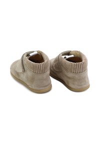 Botas de tobillo de ante en beige con tela acanalada alrededor del collar. Presentan una suela de goma plana y un cierre de gancho y lazo para facilitar el uso.