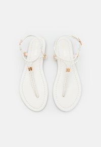 Sandales blanches à semelle plate avec des lanières tressées, des accents en métal doré et des coutures sur la semelle.