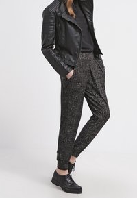 Czarna skórzana kurtka z fakturowanymi akcentami na ramionach, w połączeniu ze wzorzystymi czarnymi spodniami i czarnymi sznurowanymi butami.