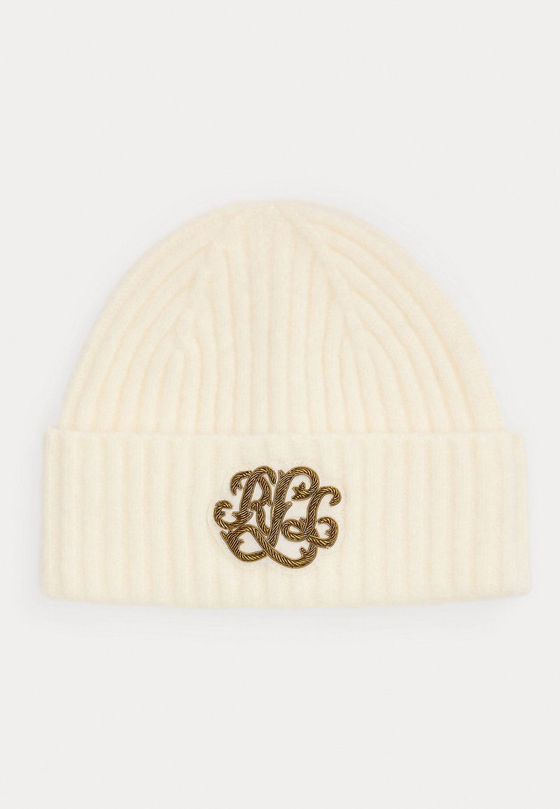 Kremkrāsas adīta beanie cepure ar ribotu tekstūru un salocītu maliņu, uz kuras ir zelta ornamentāls logo priekšpusē.