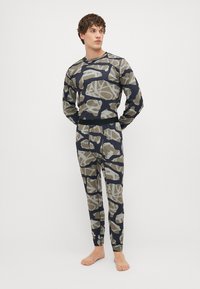 Ilgų rankovių marškiniai ir kelnių komplektas kamufliažo raštu, featuring šviesiai rudos ir tamsiai mėlynos spalvos atspalvius, pagamintas iš tamprios medžiagos su minkšta tekstūra.