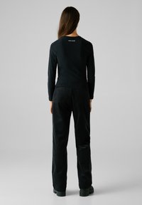 Haut à manches longues noir avec logo au dos et pantalon large en velours côtelé noir. La tenue présente une texture lisse et une silhouette ajustée.