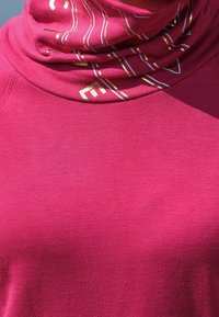 Top in tessuto fucsia con colletto alto, caratterizzato da motivi geometrici bianchi e dorati. Tessuto morbido e design aderente, adatto per essere indossato a strati.