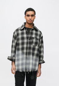 Πουκάμισο καρό ασπρόμαυρο με εφέ ombre, ξεφτισμένο τελείωμα και μία τσέπη στο στήθος. Φοριέται πάνω από μαύρο μπλουζάκι.